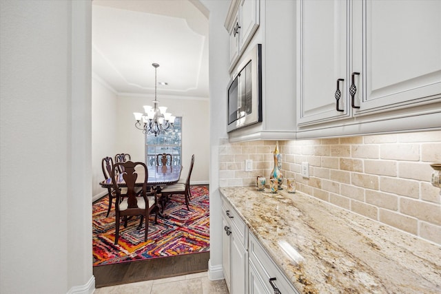 kitchen featuring stainless steel microwave, backsplash, white cabinets, ornamental molding, and light stone counters