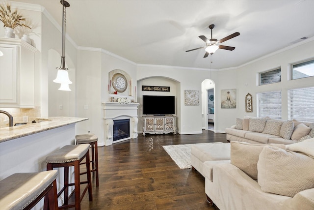 living room featuring built in shelves, crown molding, ceiling fan, and dark hardwood / wood-style floors