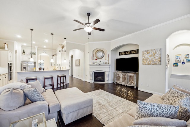 living room featuring built in shelves, ceiling fan, crown molding, and dark wood-type flooring