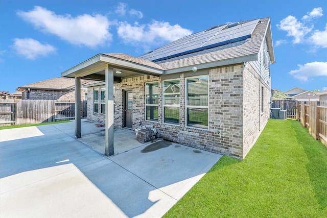 rear view of property featuring a lawn, a patio, and solar panels