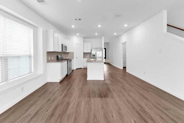 kitchen featuring stainless steel appliances, white cabinetry, a healthy amount of sunlight, and an island with sink