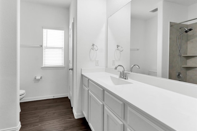 bathroom with hardwood / wood-style flooring, vanity, toilet, and tiled shower