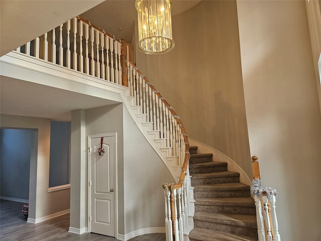 staircase with a high ceiling, hardwood / wood-style floors, and an inviting chandelier