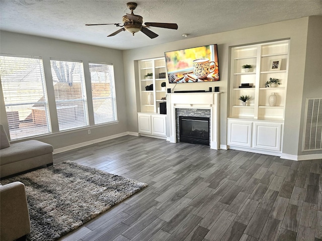 unfurnished living room featuring built in shelves, ceiling fan, dark hardwood / wood-style flooring, and a textured ceiling