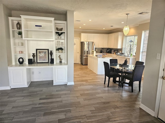 kitchen with white cabinetry, hanging light fixtures, tasteful backsplash, built in desk, and stainless steel fridge with ice dispenser