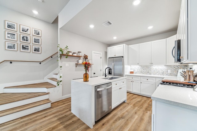 kitchen featuring white cabinets, a center island with sink, light wood-type flooring, and stainless steel appliances