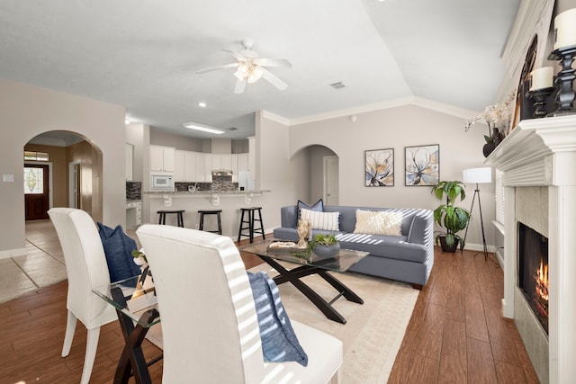 living room featuring ceiling fan, a premium fireplace, light hardwood / wood-style flooring, crown molding, and lofted ceiling