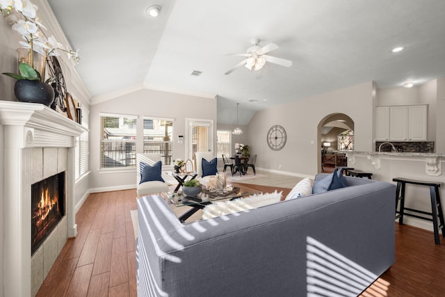 living room with a tile fireplace, ceiling fan, lofted ceiling, hardwood / wood-style flooring, and ornamental molding