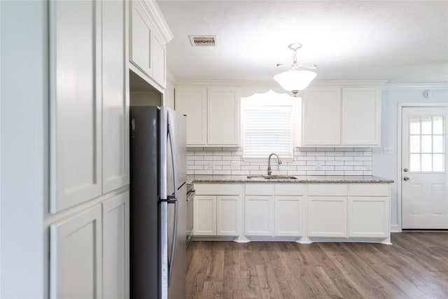 kitchen with tasteful backsplash, light stone counters, white cabinets, stainless steel fridge, and sink