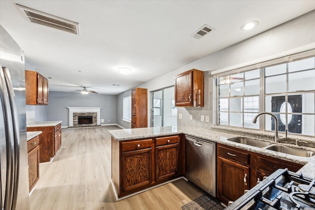 kitchen with appliances with stainless steel finishes, a fireplace, sink, kitchen peninsula, and light wood-type flooring