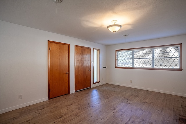 unfurnished bedroom featuring hardwood / wood-style flooring, a textured ceiling, and multiple closets