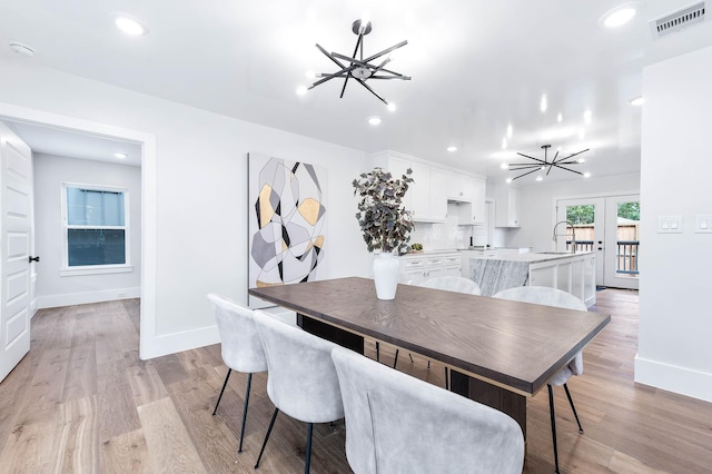 dining room featuring sink, light wood-type flooring, french doors, and a chandelier