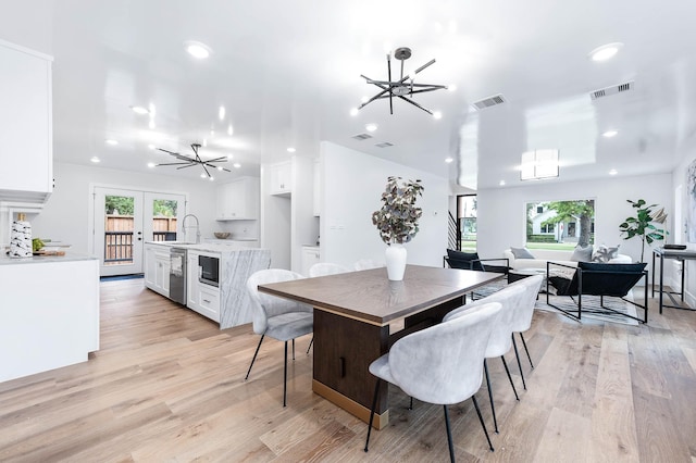 dining area with an inviting chandelier, french doors, sink, and light hardwood / wood-style flooring