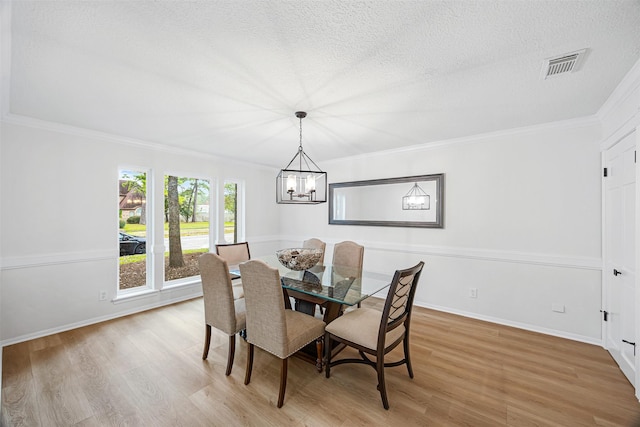 dining area featuring a textured ceiling, light hardwood / wood-style floors, ornamental molding, and a notable chandelier