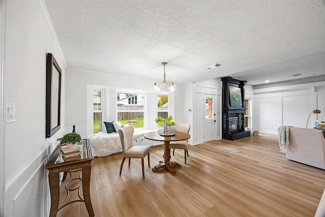 dining area with light hardwood / wood-style flooring, crown molding, a chandelier, a textured ceiling, and a fireplace