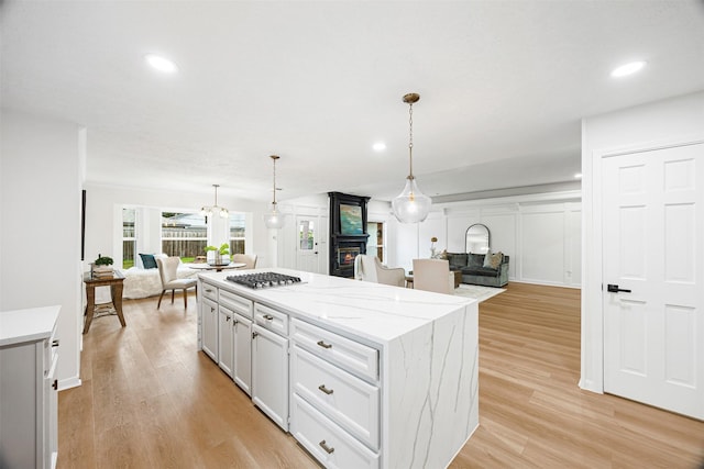 kitchen featuring a kitchen island, light hardwood / wood-style flooring, pendant lighting, stainless steel gas stovetop, and white cabinets