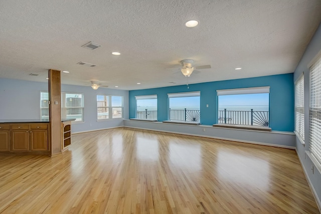 unfurnished living room with ceiling fan, a textured ceiling, and light hardwood / wood-style flooring