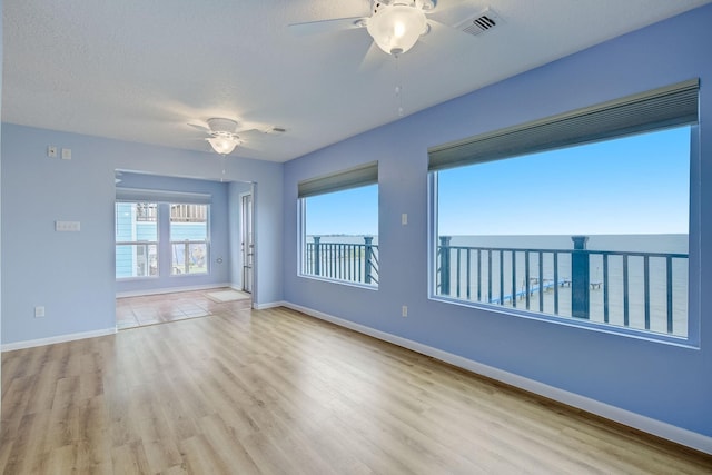 spare room with a textured ceiling, a water view, ceiling fan, and light hardwood / wood-style floors