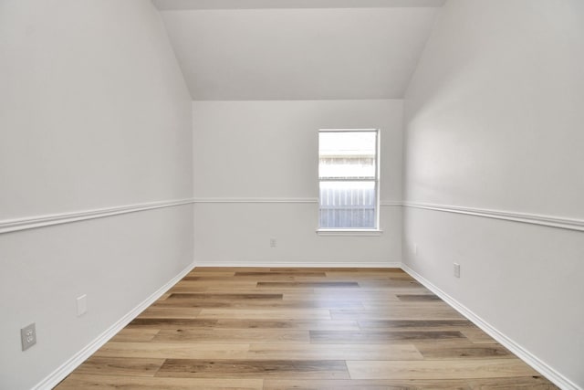 spare room featuring light wood-type flooring and vaulted ceiling