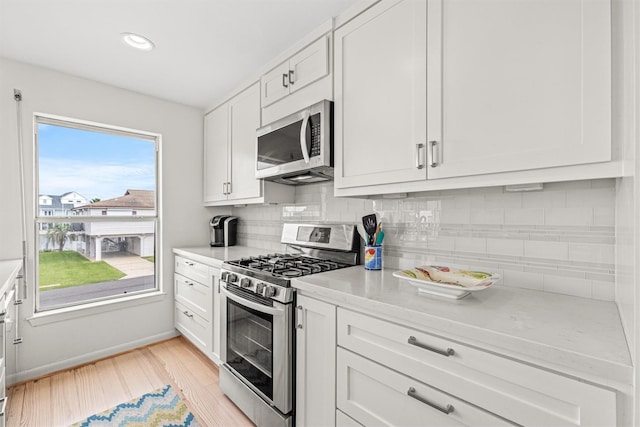 kitchen with white cabinetry, light stone countertops, light hardwood / wood-style flooring, backsplash, and appliances with stainless steel finishes