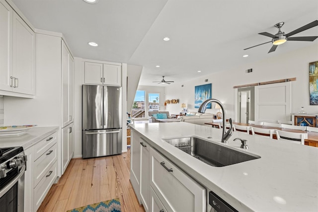 kitchen with white cabinets, sink, light hardwood / wood-style flooring, a barn door, and appliances with stainless steel finishes