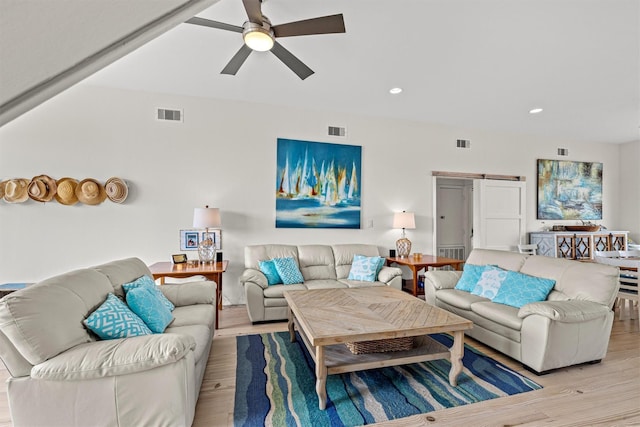 living room with ceiling fan, a barn door, and light hardwood / wood-style floors