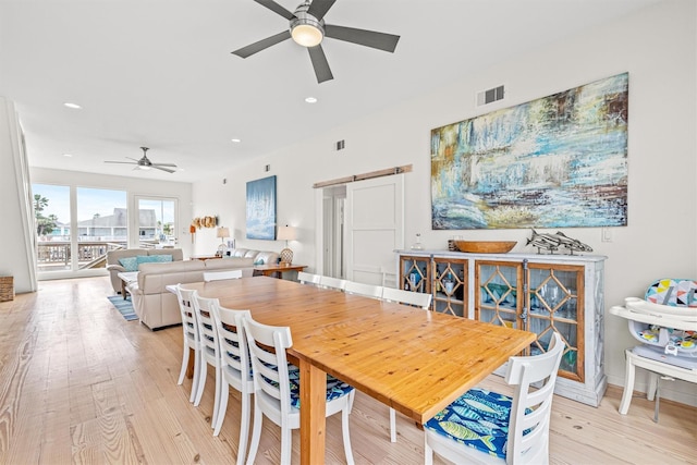 dining room featuring light wood-type flooring, a barn door, and ceiling fan