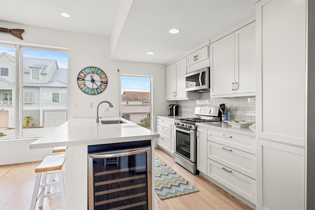 kitchen featuring sink, beverage cooler, light hardwood / wood-style flooring, white cabinets, and appliances with stainless steel finishes