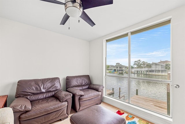 sitting room with ceiling fan, a water view, and wood-type flooring