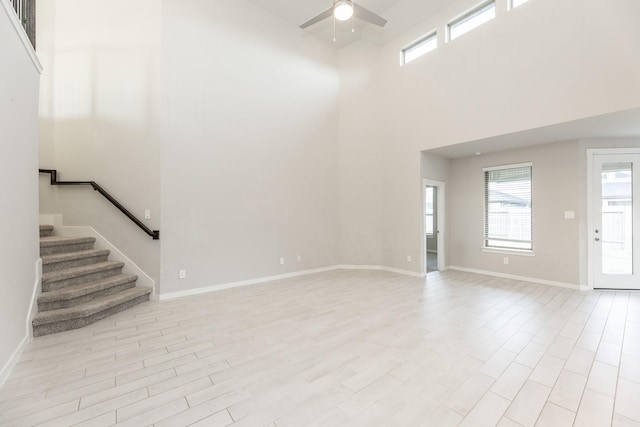 unfurnished living room with ceiling fan, a towering ceiling, and light hardwood / wood-style flooring