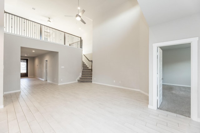 unfurnished living room featuring ceiling fan and a towering ceiling