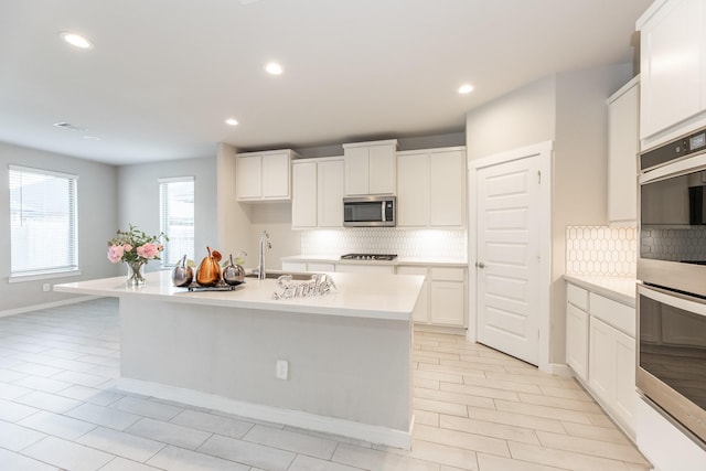 kitchen featuring sink, backsplash, a center island with sink, white cabinets, and appliances with stainless steel finishes