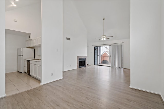 unfurnished living room featuring a tiled fireplace, high vaulted ceiling, light hardwood / wood-style floors, and ceiling fan