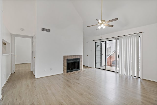 unfurnished living room with ceiling fan, a tiled fireplace, high vaulted ceiling, and light wood-type flooring