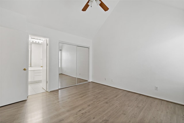 unfurnished bedroom featuring ensuite bathroom, high vaulted ceiling, light hardwood / wood-style flooring, ceiling fan, and a closet