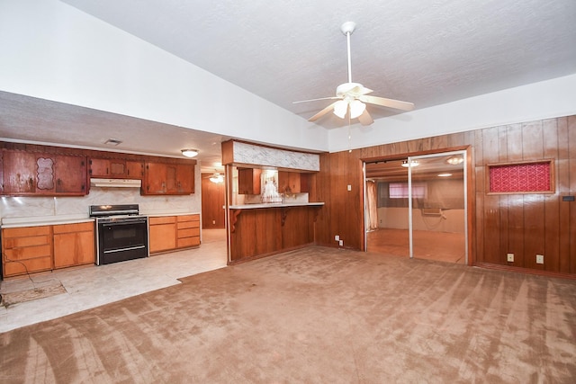 kitchen with wood walls, backsplash, black range, light colored carpet, and kitchen peninsula