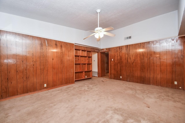 carpeted empty room featuring ceiling fan and wood walls