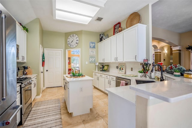 kitchen with stainless steel appliances, a kitchen island, white cabinetry, and kitchen peninsula