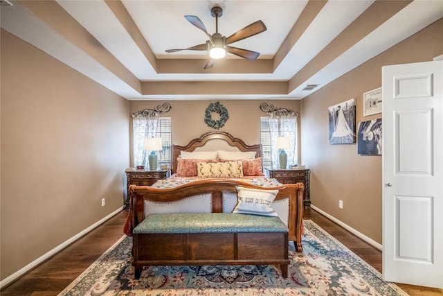 bedroom featuring dark hardwood / wood-style flooring, ceiling fan, and a raised ceiling