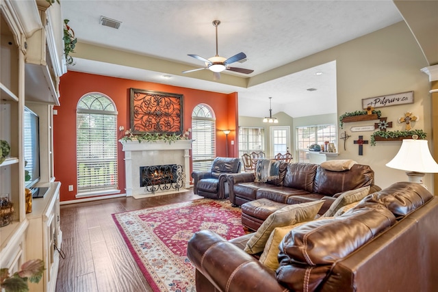 living room featuring a fireplace, ceiling fan with notable chandelier, a tray ceiling, and dark hardwood / wood-style flooring