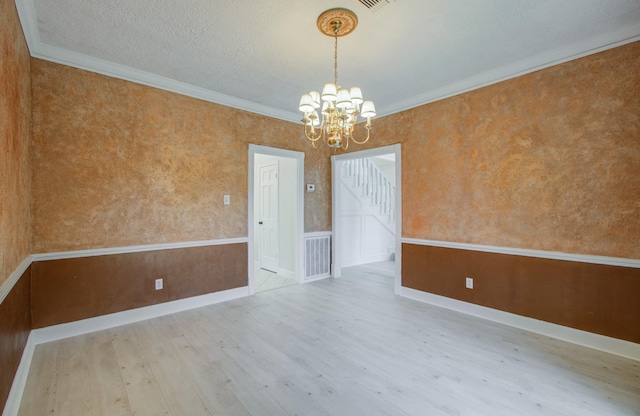 spare room with light hardwood / wood-style flooring, an inviting chandelier, a textured ceiling, and ornamental molding