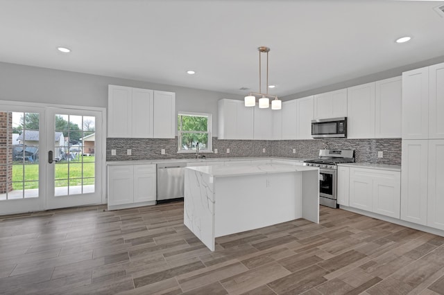 kitchen featuring stainless steel appliances, a kitchen island, a wealth of natural light, and white cabinetry