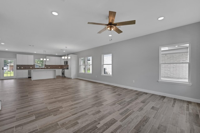 unfurnished living room featuring ceiling fan with notable chandelier, light hardwood / wood-style floors, and sink