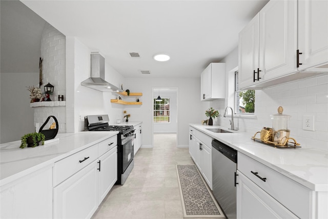 kitchen featuring light stone countertops, appliances with stainless steel finishes, sink, wall chimney range hood, and white cabinets