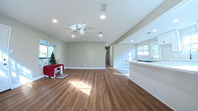 unfurnished living room featuring ceiling fan, sink, dark wood-type flooring, and a wealth of natural light