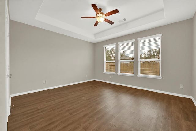 empty room with dark hardwood / wood-style floors, ceiling fan, and a tray ceiling