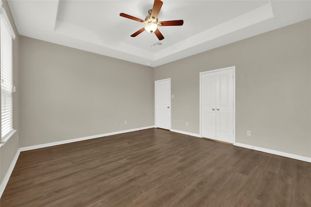 spare room featuring dark hardwood / wood-style flooring, ceiling fan, and a raised ceiling