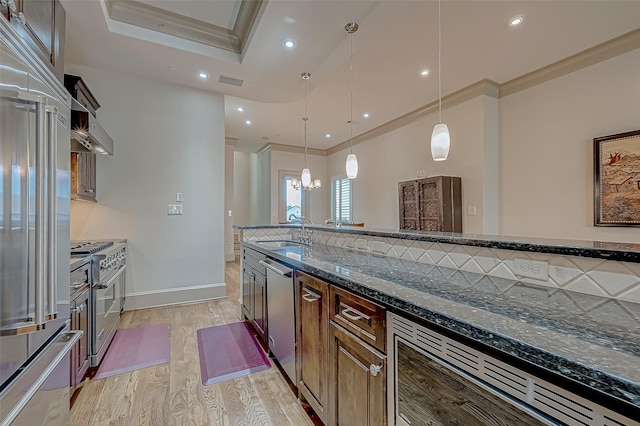 kitchen featuring light wood-type flooring, dark stone counters, high end appliances, sink, and pendant lighting