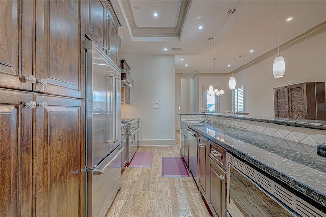 kitchen featuring sink, light hardwood / wood-style flooring, dark stone counters, decorative light fixtures, and appliances with stainless steel finishes