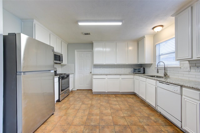 kitchen with light stone countertops, sink, stainless steel appliances, backsplash, and white cabinets